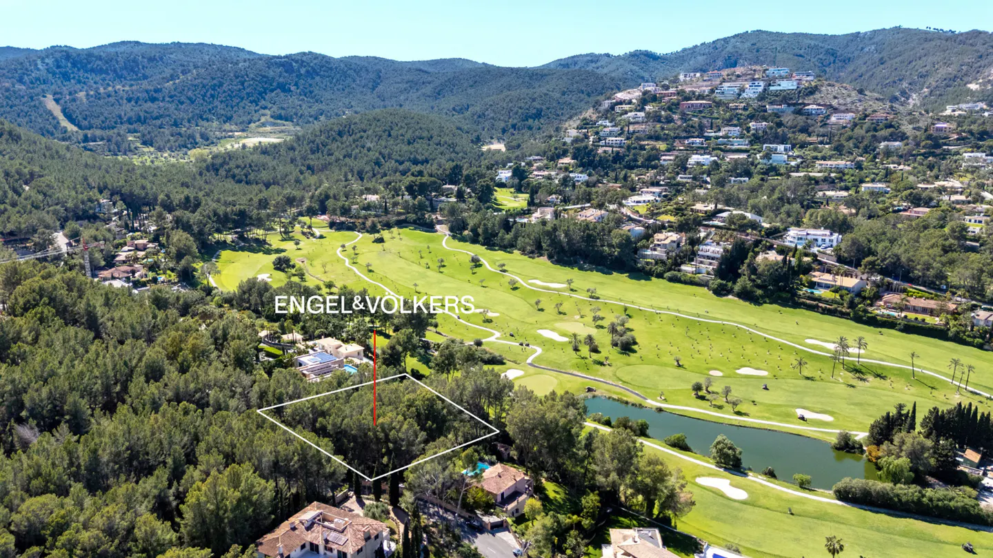 Aerial view of a wooded lot outlined in white, near a golf course and lake, with mountains in the background. Engel & Volkers logo visible.
