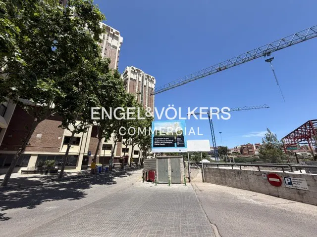 Construction site with tall buildings, a crane, and a blue information sign under a clear blue sky.