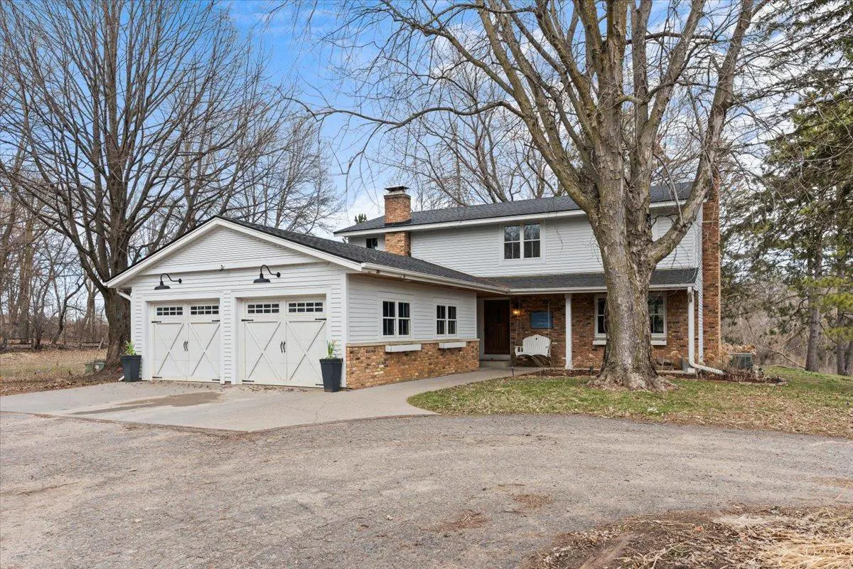 Two-story house with a two-car garage, brick accents, and a white porch swing. Bare trees surround the property.