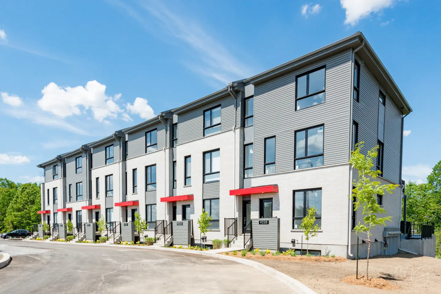 Row of modern townhouses with gray siding, white brick, black windows, and red awnings under a blue sky.