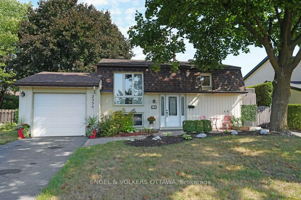 A two-story house with a brown roof, white siding, and a white garage door. A tree is in the front yard.