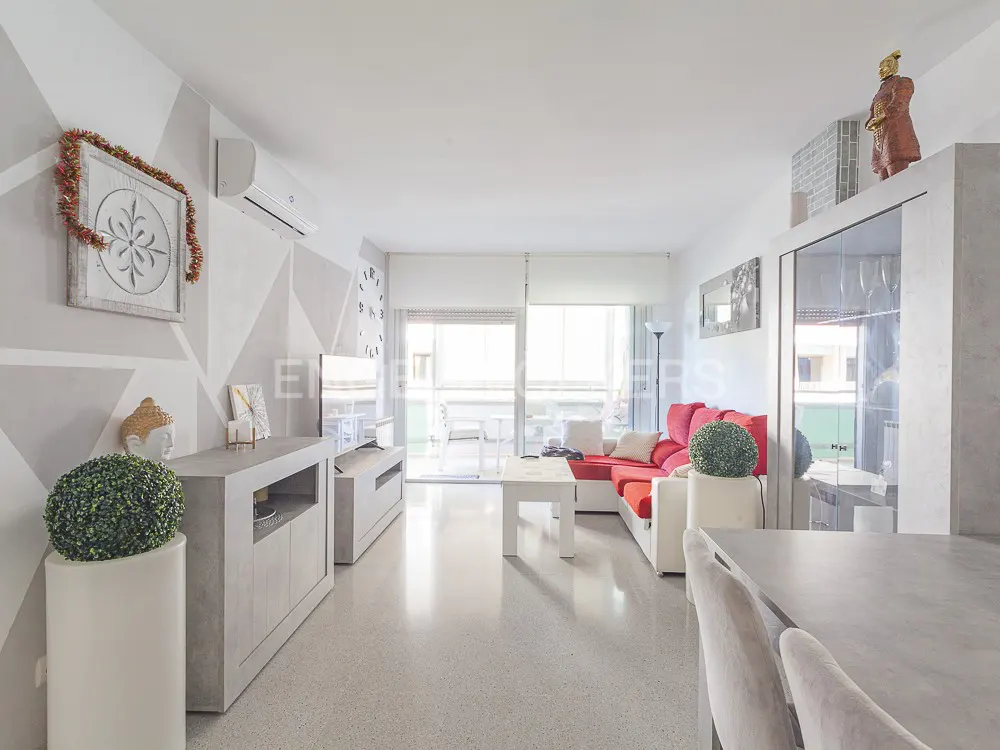 Bright living room with white walls, gray accents, and a red sofa. A balcony is visible through sliding glass doors.