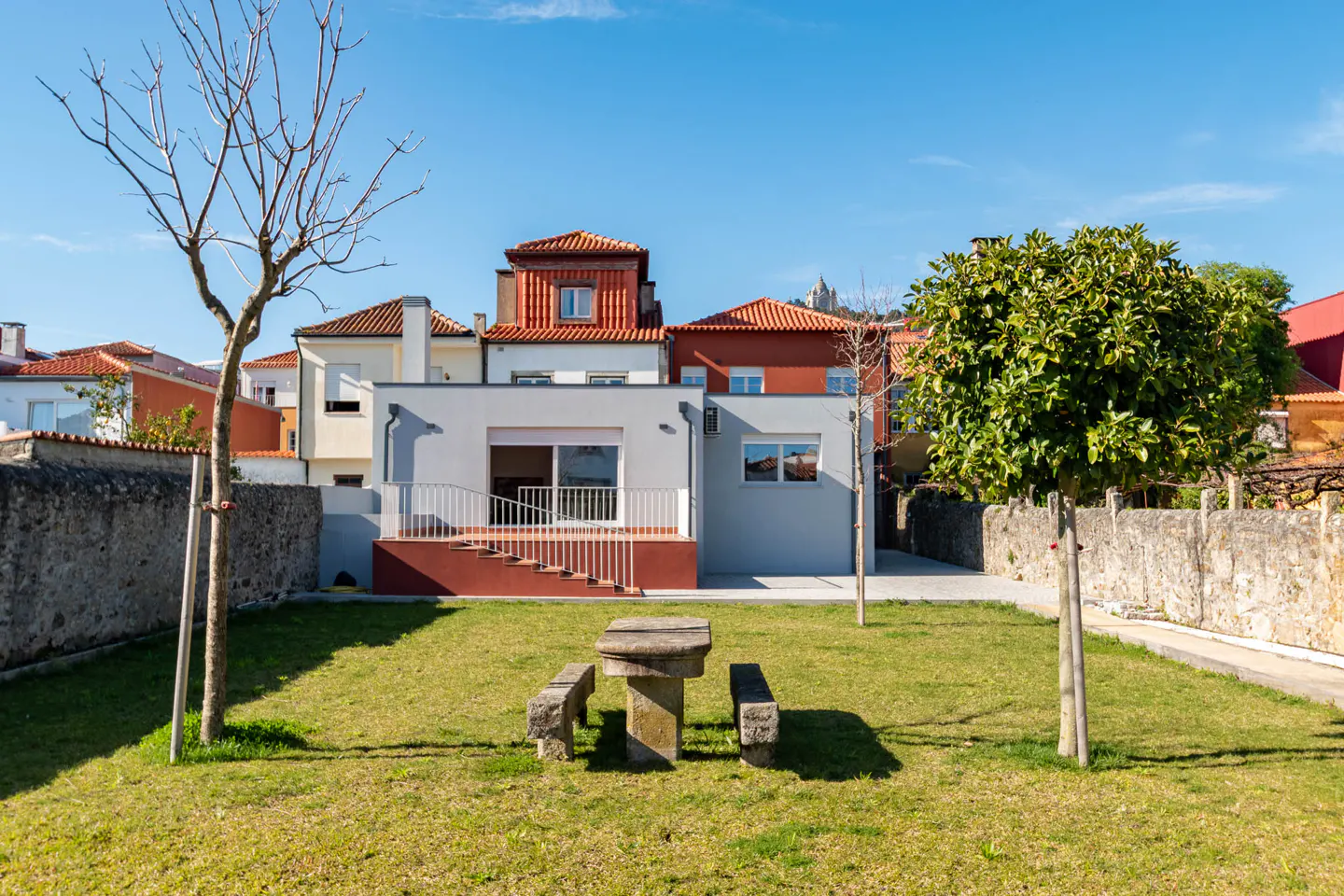Backyard view of a modern grey house with a stone picnic table on the green lawn.