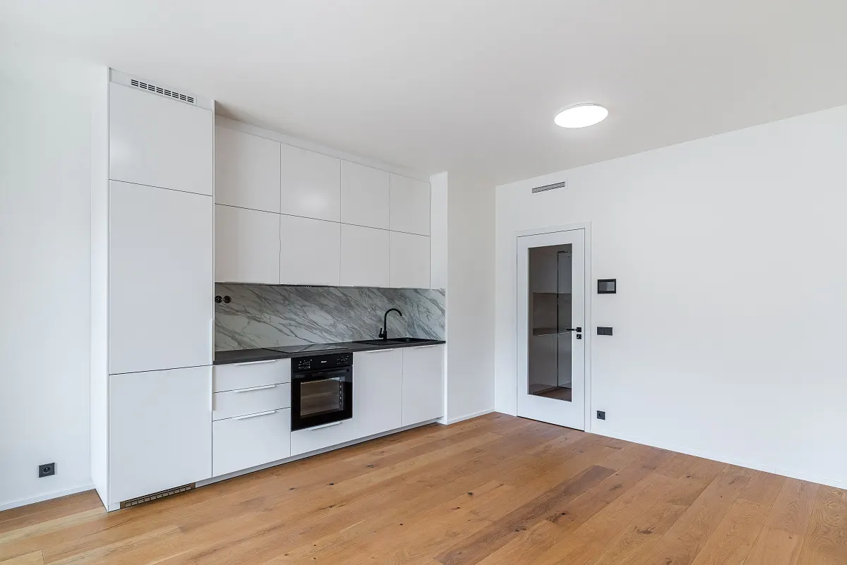 Bright, modern kitchen with white cabinets, marble backsplash, and black appliances. Hardwood floors and a glass-paneled door add warmth.