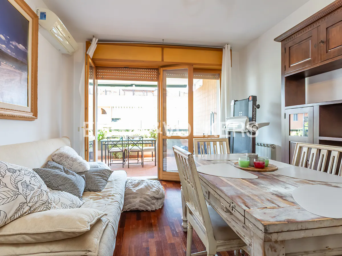 Living room with a white sofa, wooden table, and open balcony doors leading to an outdoor seating area.