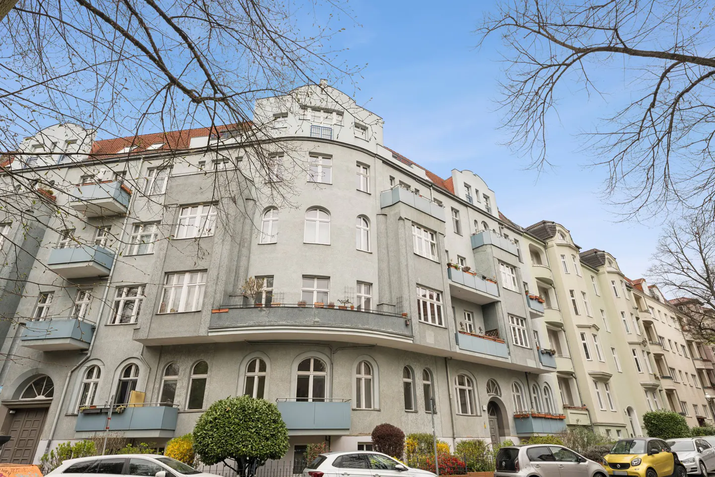 Exterior view of a multi-story gray apartment building with white windows and small balconies under a blue sky.