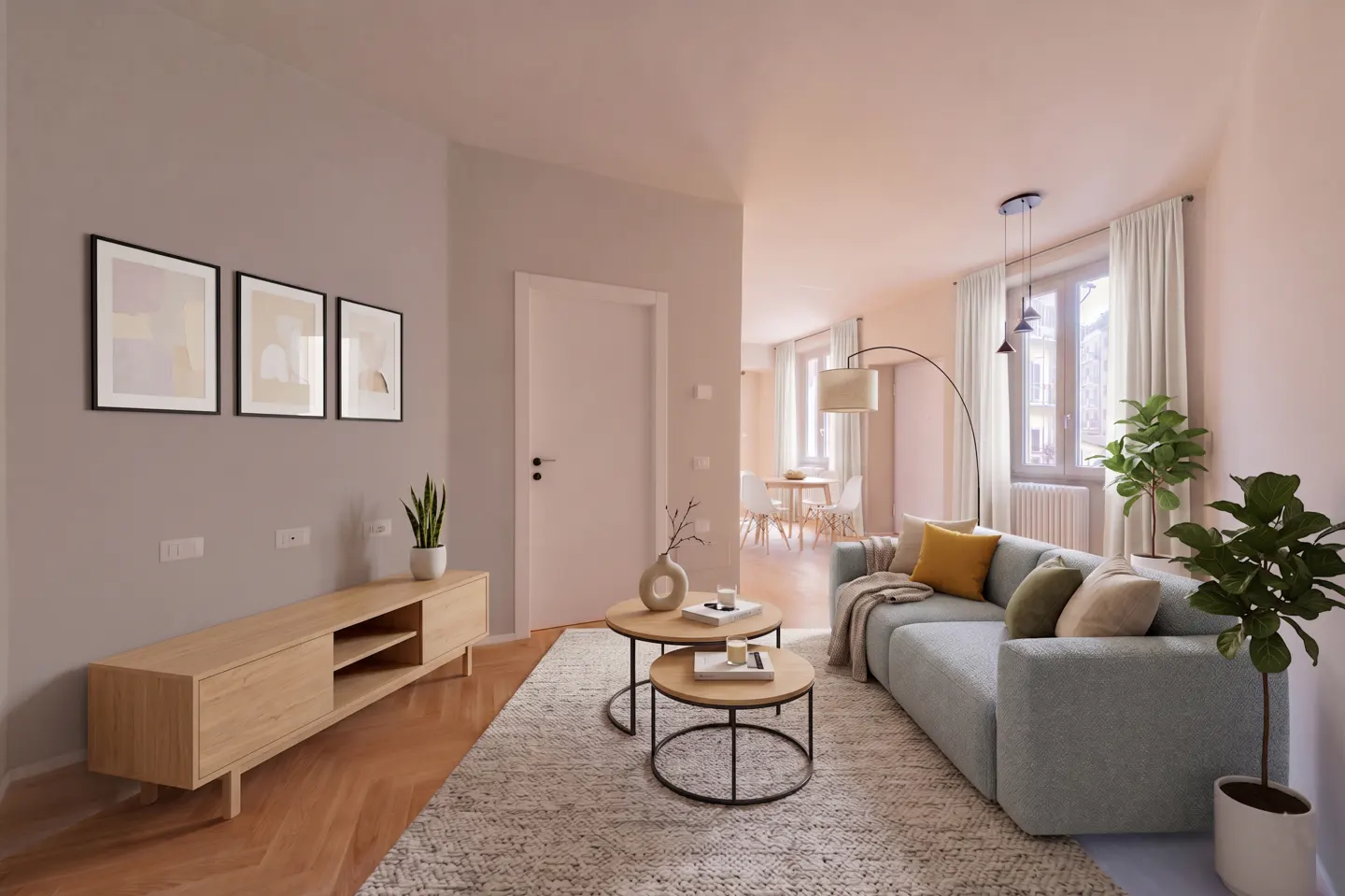 Living room with a light blue sofa, wooden TV stand, and round coffee tables on a patterned rug. Three framed artworks hang on the wall.