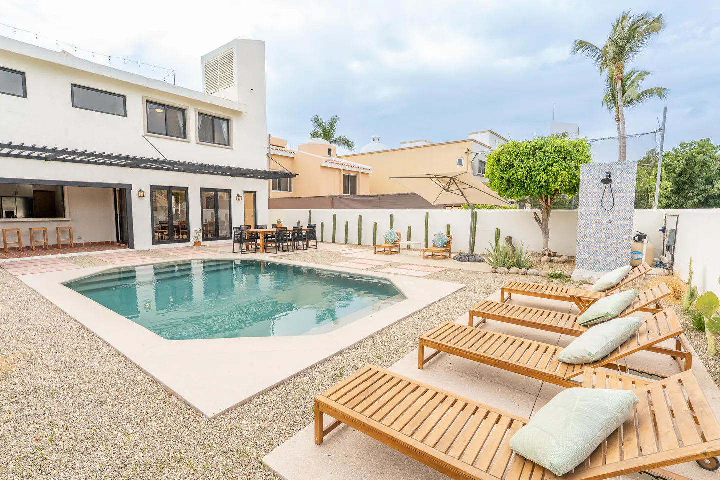 Backyard with a pool, lounge chairs, and outdoor shower. A white house with black trim is in the background.
