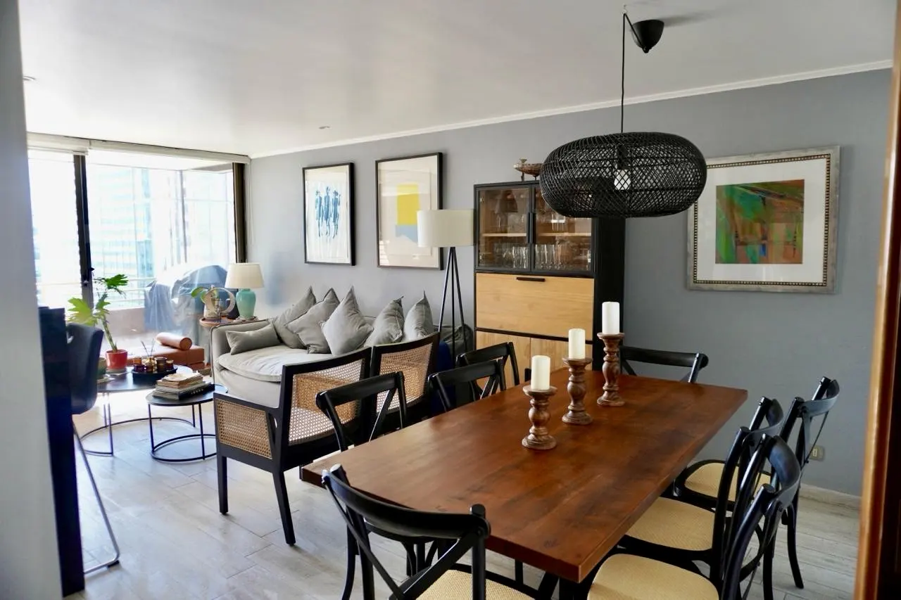 Living and dining area with gray walls, wood table with candles, black chairs, and a sofa with pillows. Balcony with city view.