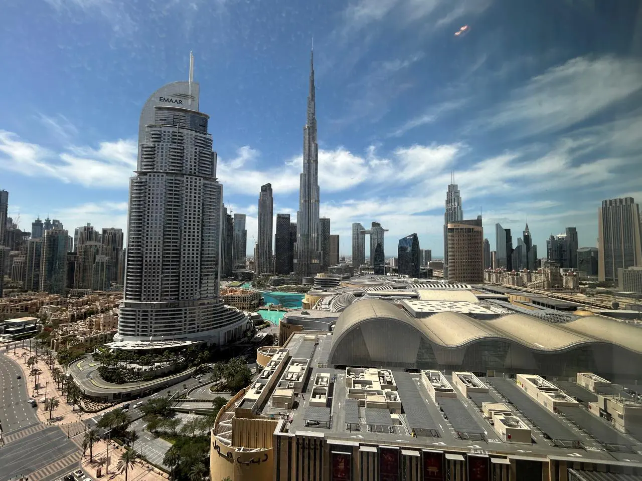 Dubai skyline view featuring the Burj Khalifa, Emaar building, and Dubai Mall under a blue sky with scattered clouds.
