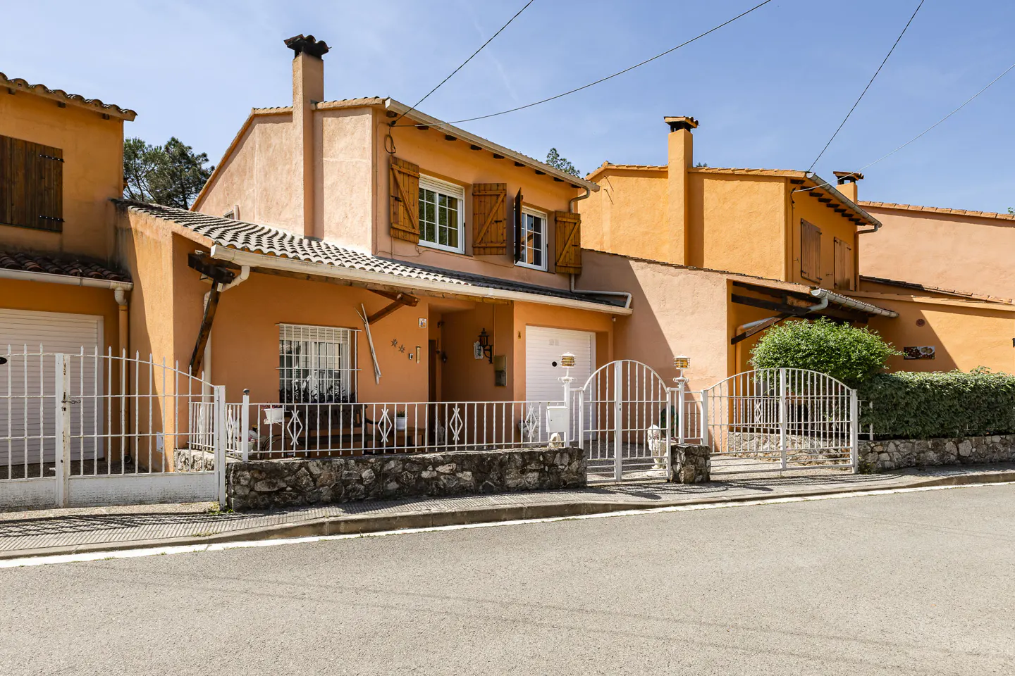 Exterior view of orange townhouses with white fences and brown shutters under a clear blue sky.