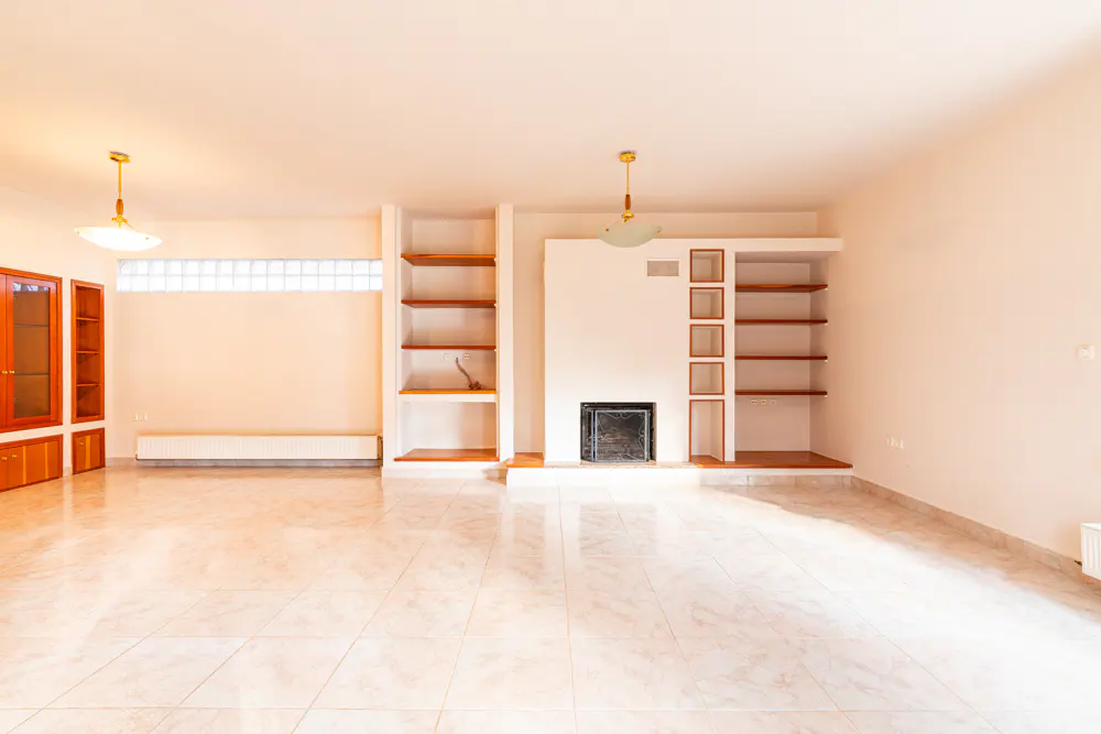 Spacious living room with light tile floors, a central fireplace, built-in wooden shelving, and two pendant light fixtures.
