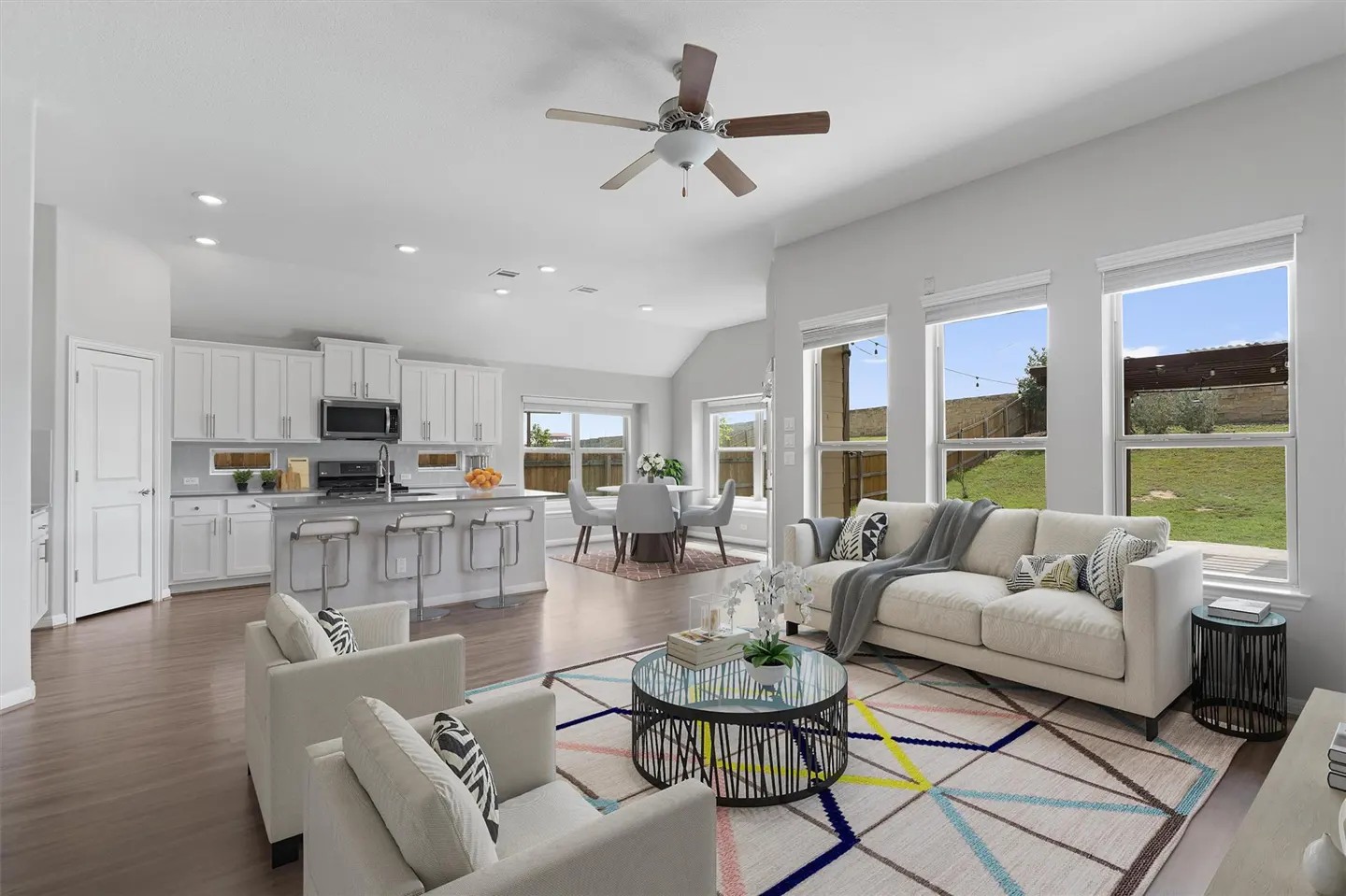 Open-concept living space with white kitchen, dining area, and living room. Large windows overlook a green lawn.
