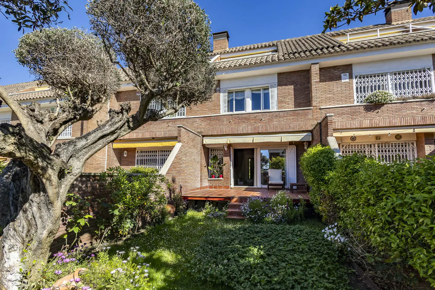 Exterior view of a red brick townhouse with a garden and a wooden deck.