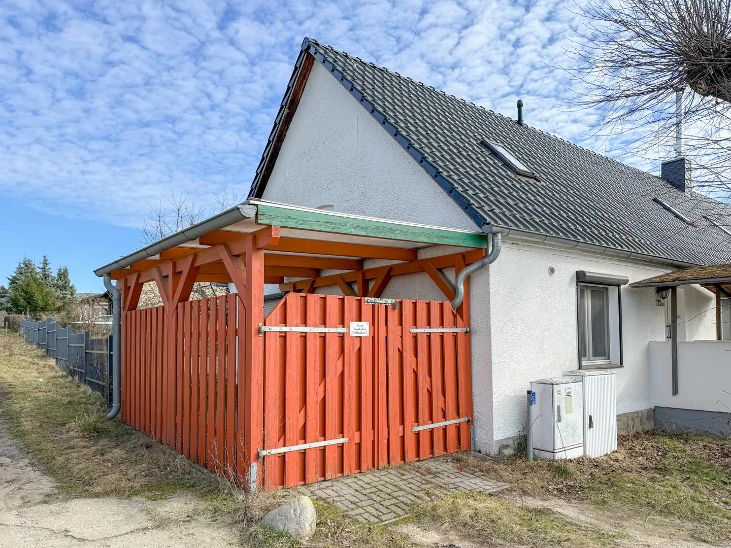 Exterior view of a white house with a gray roof and an orange wooden fence.