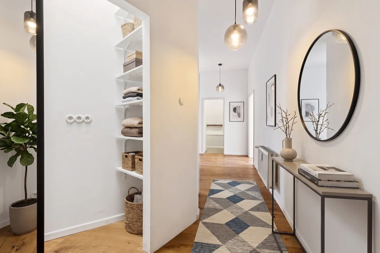 Bright hallway with hardwood floors, geometric rug, open shelving, console table with mirror, and modern pendant lighting.