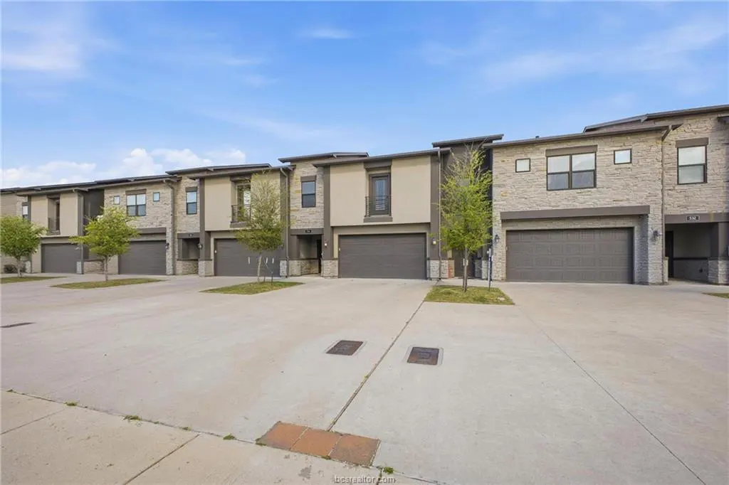Row of modern townhouses with gray garages and stone and beige facades under a blue sky.