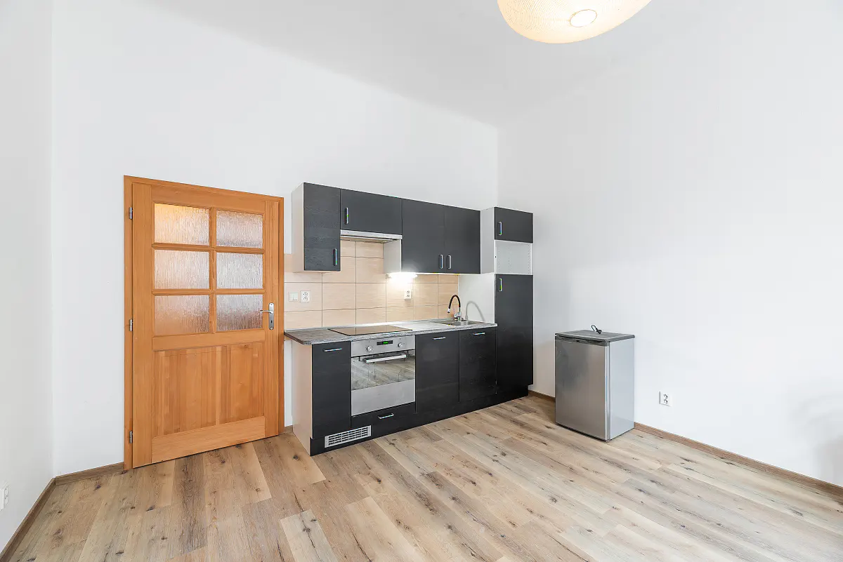 A small kitchen with black cabinets, a stainless steel mini-fridge, and a light wood door.