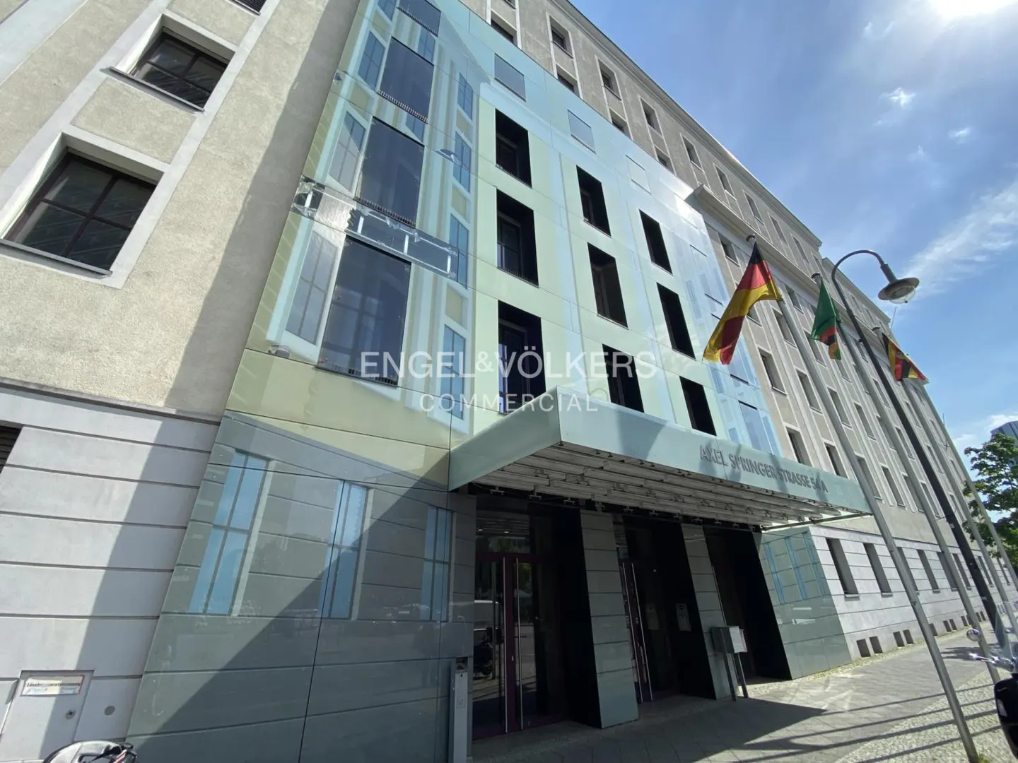 Exterior view of Engel & Völkers Commercial building with flags. The building is light gray with dark windows and a modern glass facade.