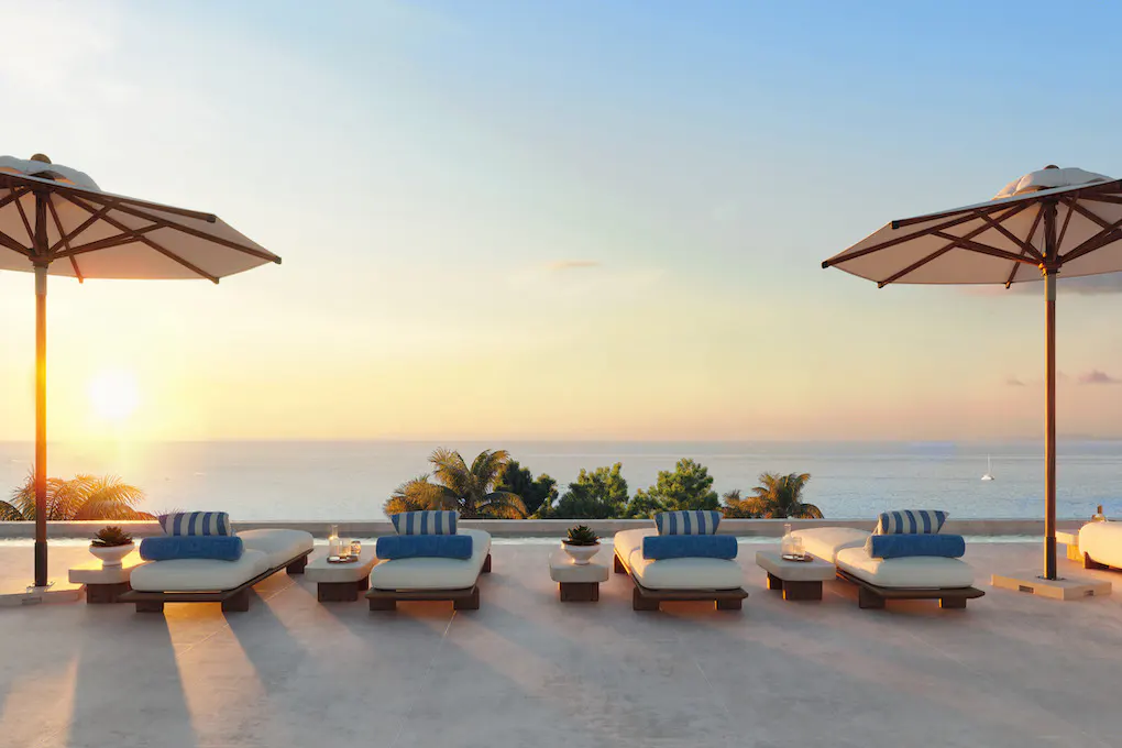 Luxury patio with lounge chairs and umbrellas overlooking the ocean at sunset.
