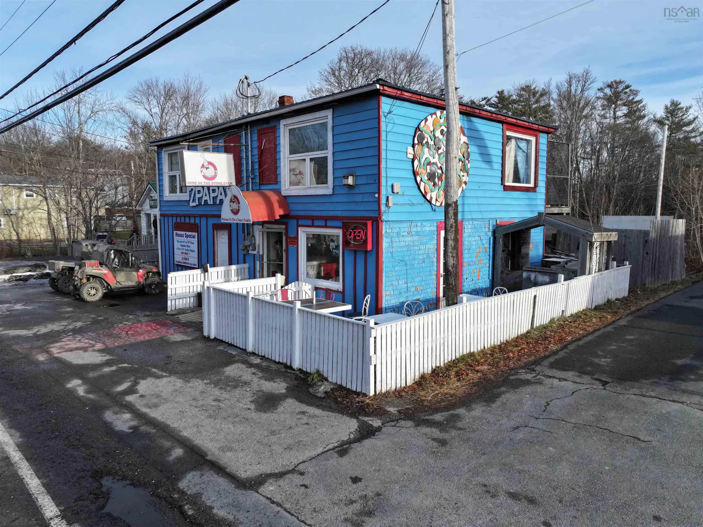 Two-story blue building with red trim and a white picket fence. A sign reads "Papa" above the entrance. An ATV is parked nearby.
