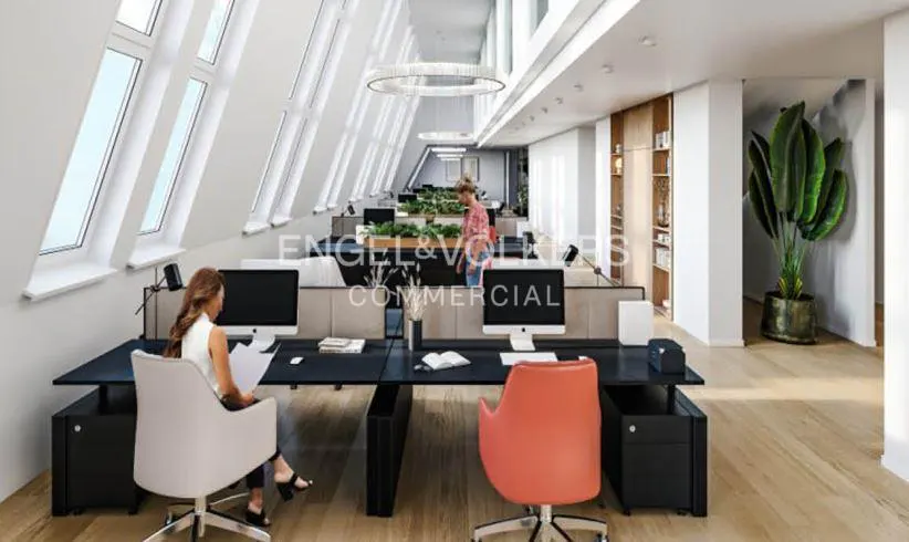 Bright office space with black desks, computers, and colorful chairs. Large windows and a plant add to the modern design.