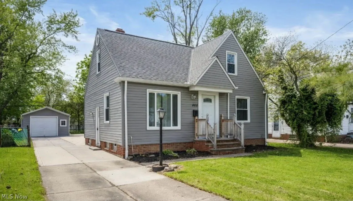 Exterior of a gray two-story house with a white door, gray roof, green lawn, and a detached garage.