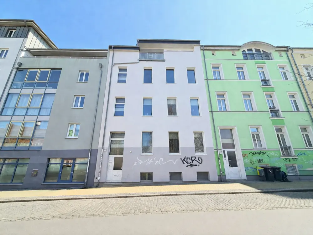 Three-story buildings in a row, painted gray, white, and green, with graffiti on the lower walls.