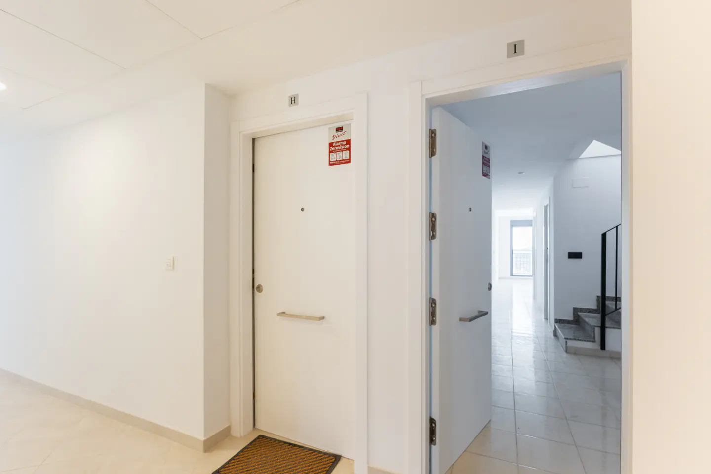 Hallway with two white doors, one closed with a brown mat, and the other open revealing a staircase.
