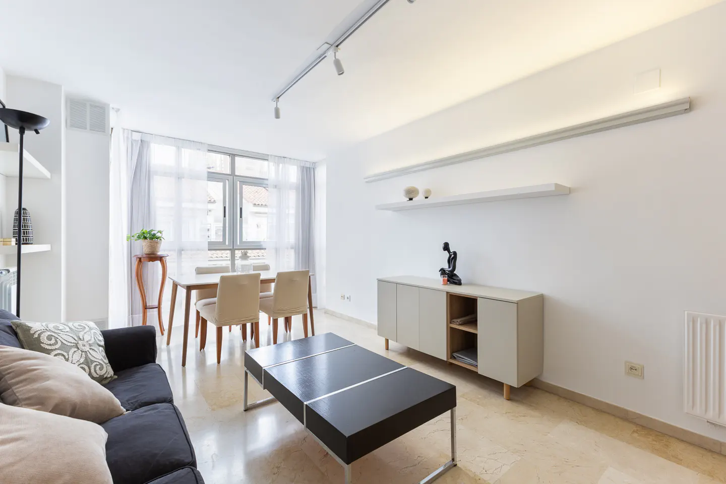 Bright living room with a black sofa, dining table, and a modern black coffee table on a marble floor.
