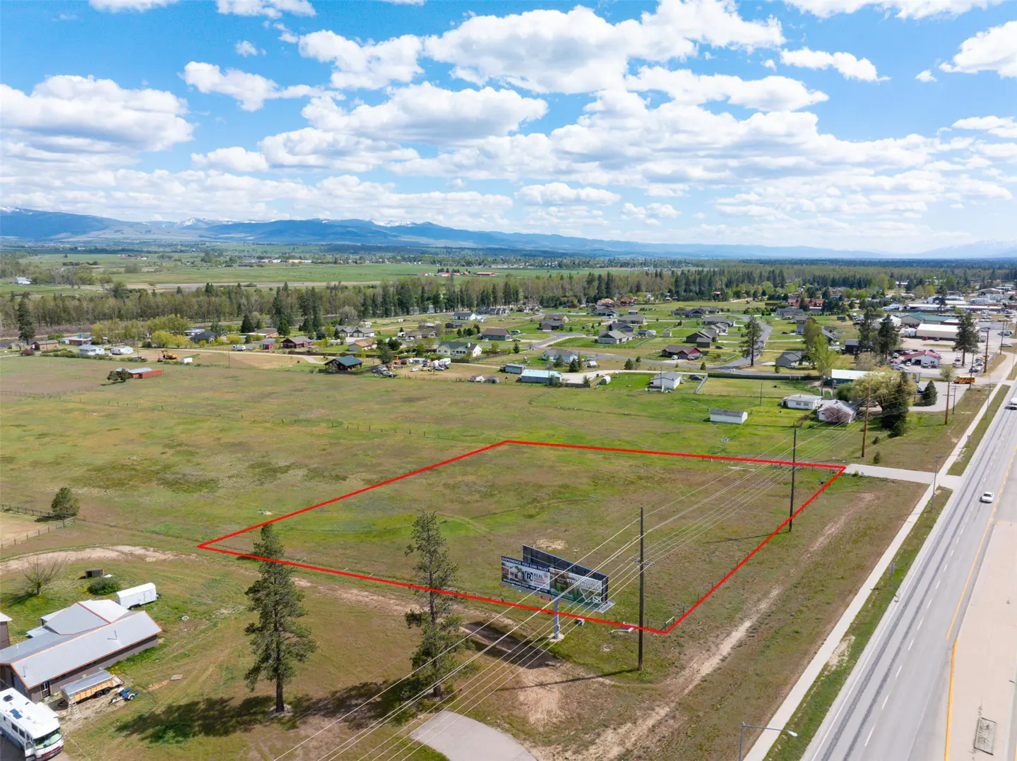 Aerial view of a large, grassy lot outlined in red, with mountains in the background and a highway to the right.