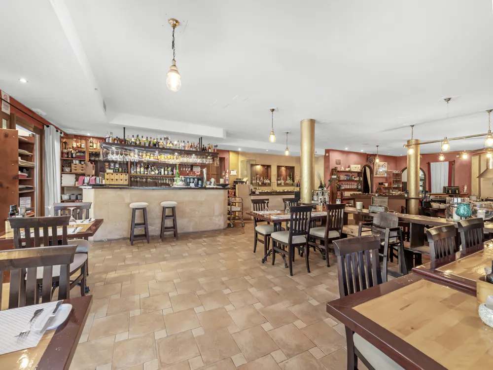 Interior of a restaurant with a bar, tables, and chairs. The floor is tiled, and the walls are painted in warm colors.