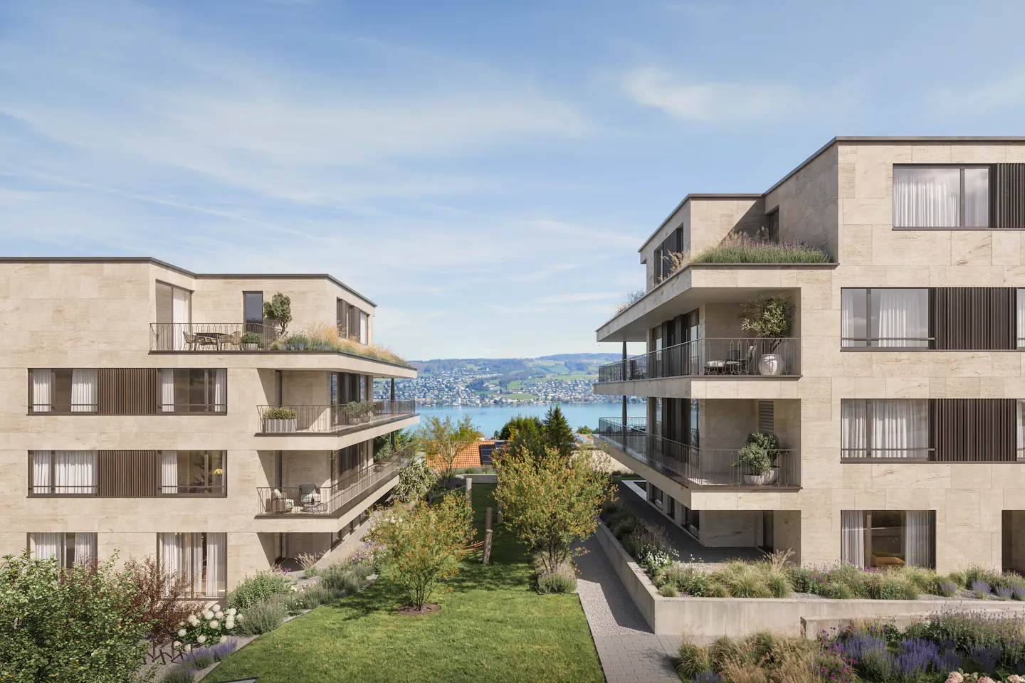 Two modern stone apartment buildings face each other with a green lawn and lake view under a blue sky.