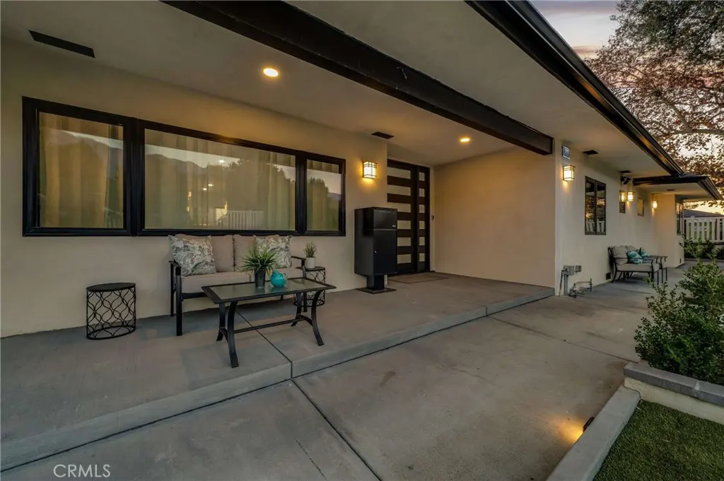 Exterior view of a modern home with a concrete porch, black framed windows, and a black front door. A sofa and table sit on the porch.