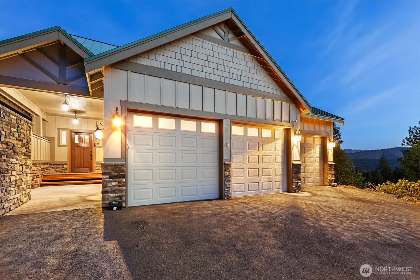 Exterior of a modern home at dusk with a three-car garage, stone accents, and a wooden front door under warm lighting.