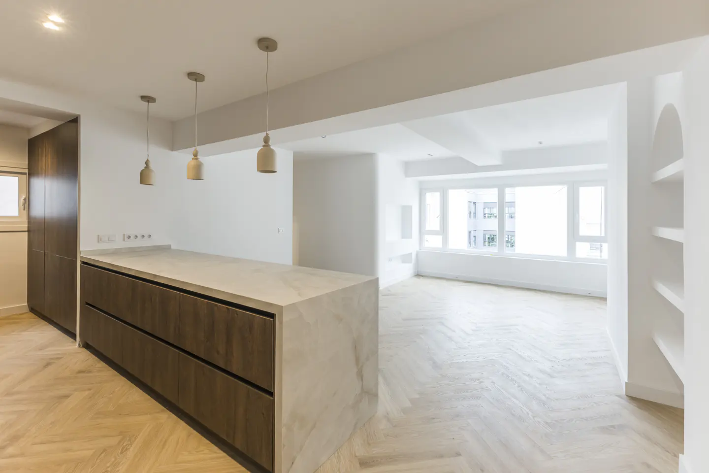 Bright, modern kitchen with wood cabinets, marble countertop island, and pendant lights. Open floor plan leads to a living area with large windows.