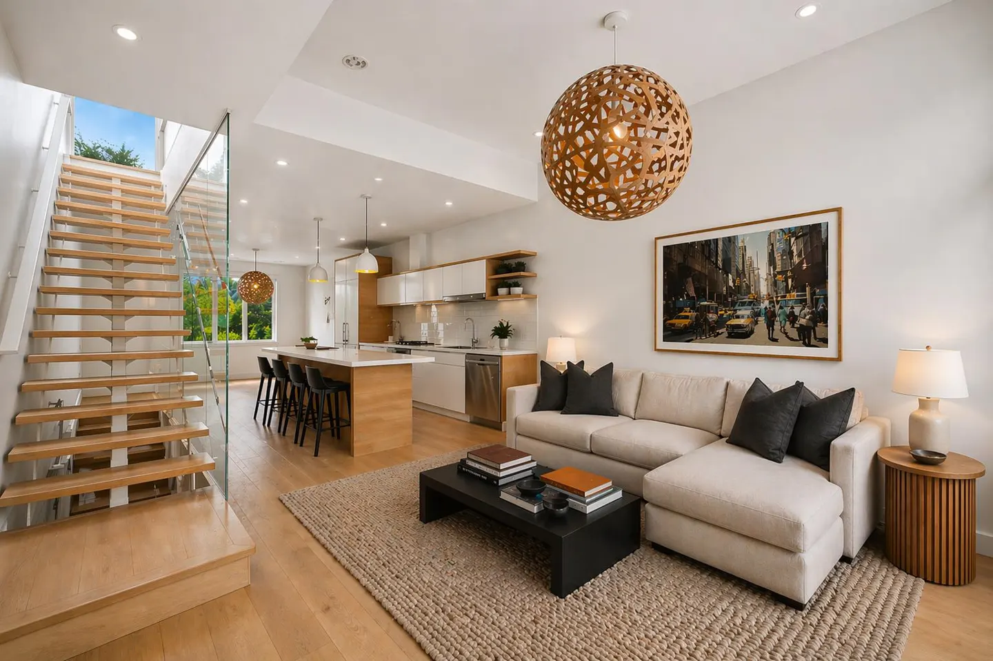 Open-concept living space with wood floors, a staircase with glass railing, a kitchen island, and a beige sectional sofa.