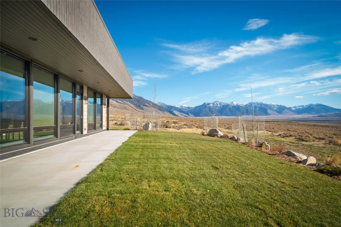 Exterior view of a modern home with large windows, green lawn, and mountain views under a blue sky.