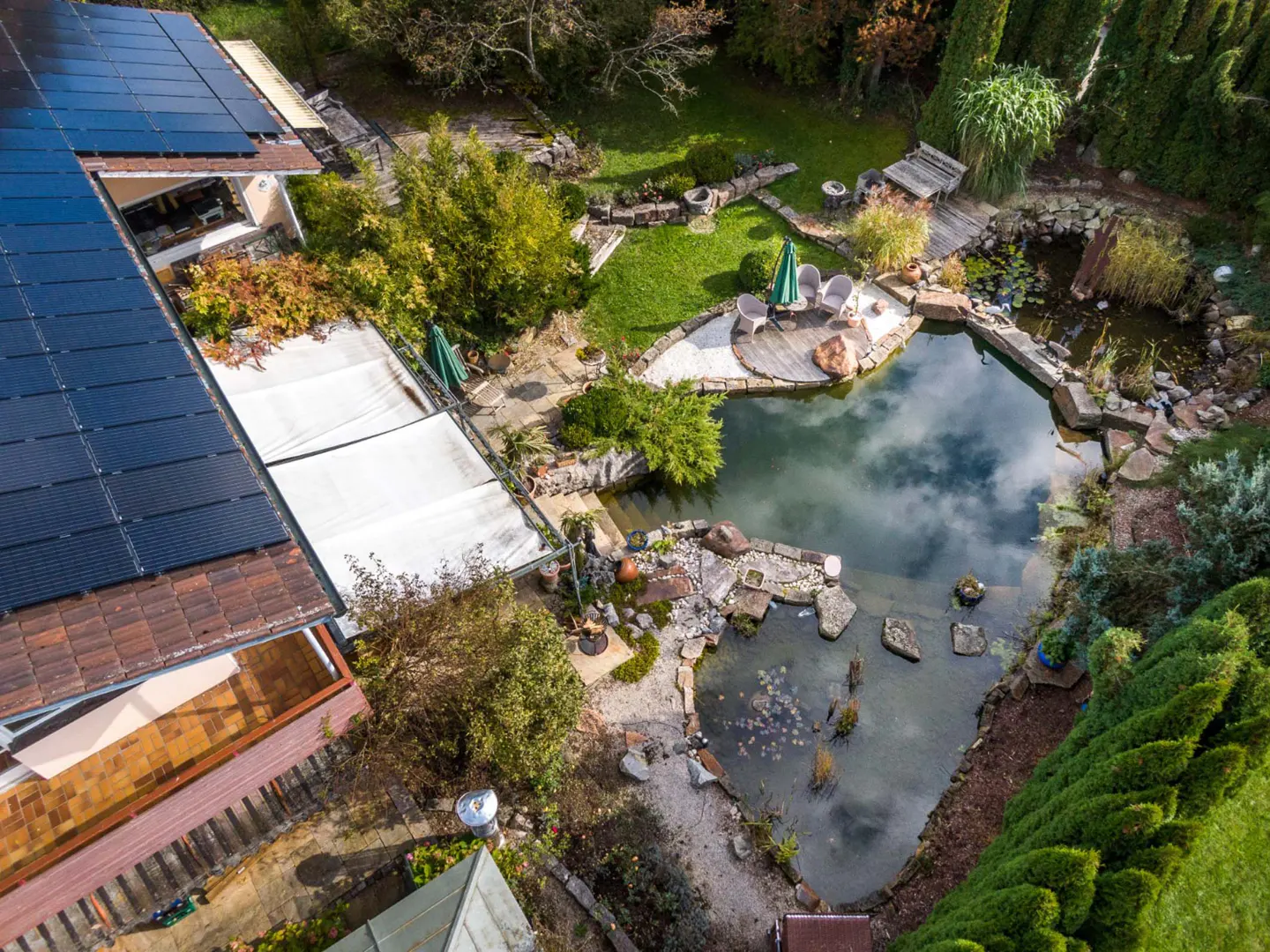 Aerial view of a house with solar panels and a backyard pond with a seating area.