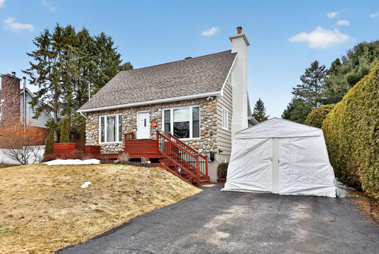 A stone and siding house with a red porch and stairs, a white door, and a white tent-like structure in the driveway.