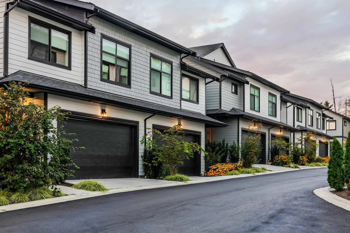 Row of modern townhouses with gray siding, black trim, and dark garage doors along a curved driveway.