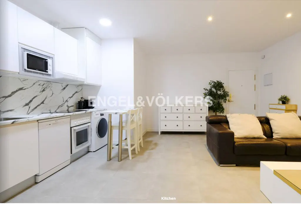 Bright, open-concept apartment with white kitchen cabinets, marble backsplash, and a brown leather sofa. Engel & Völkers logo visible.