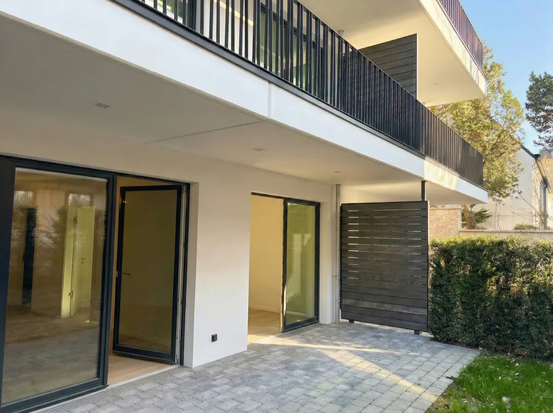 Exterior view of a modern two-story building with a balcony, sliding glass doors, and a gray brick patio.