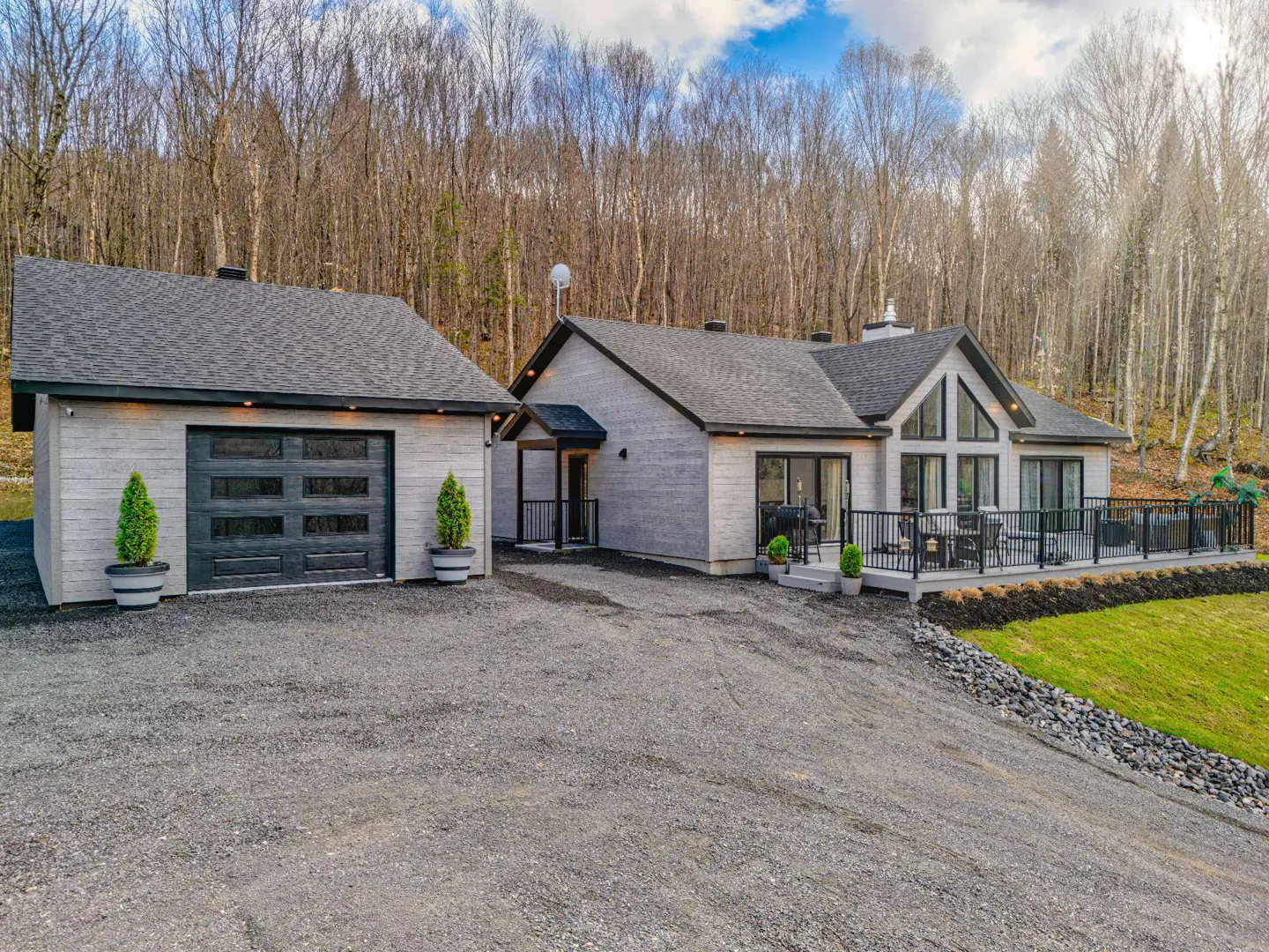Exterior of a modern gray house with a black garage door and a large deck. Trees in the background.