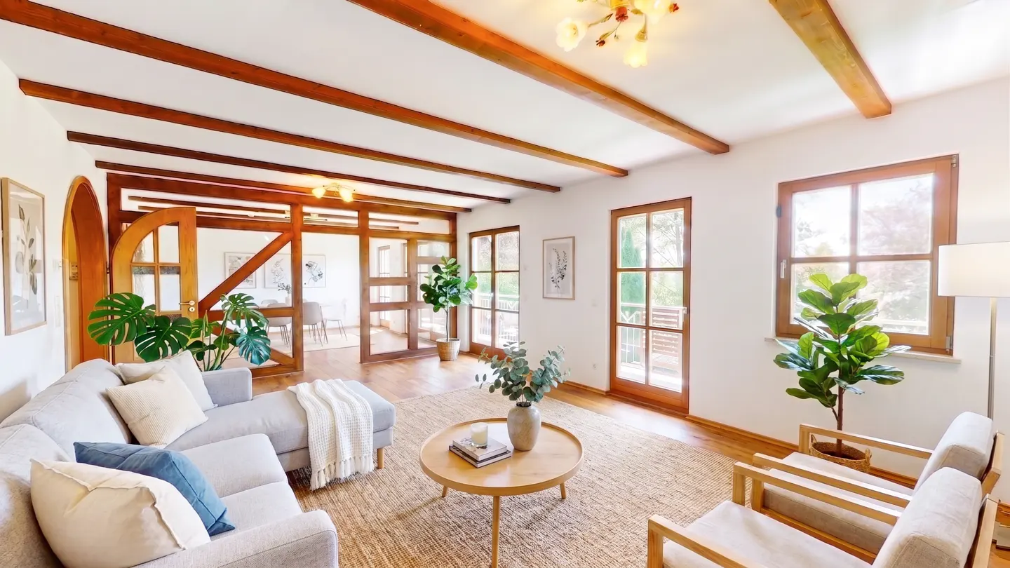 Bright living room with wood beams, light gray sectional, round wood table, and two wood-framed chairs on a jute rug.