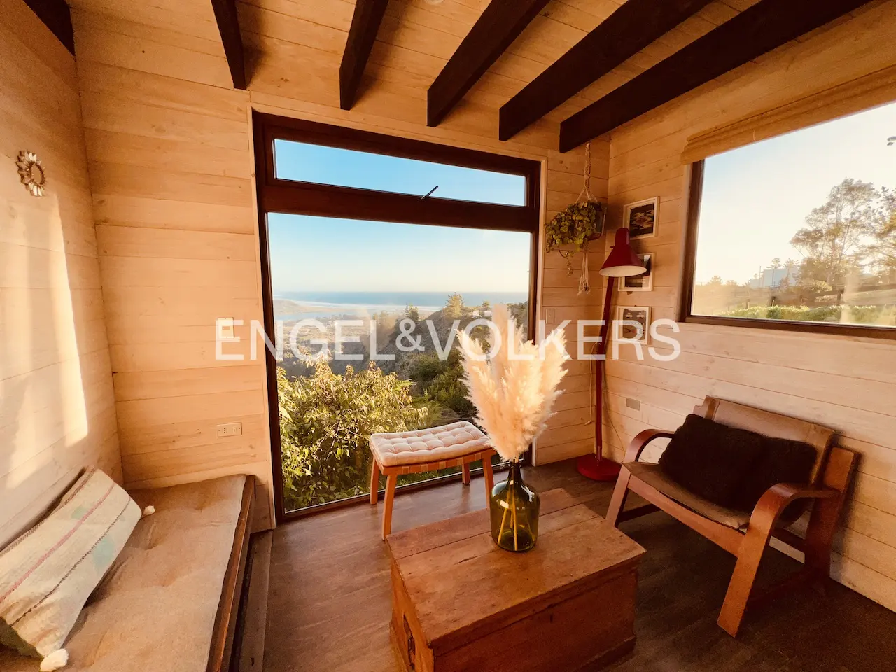 A cozy room with wood walls, a bench, a chair, and a large window with an ocean view.