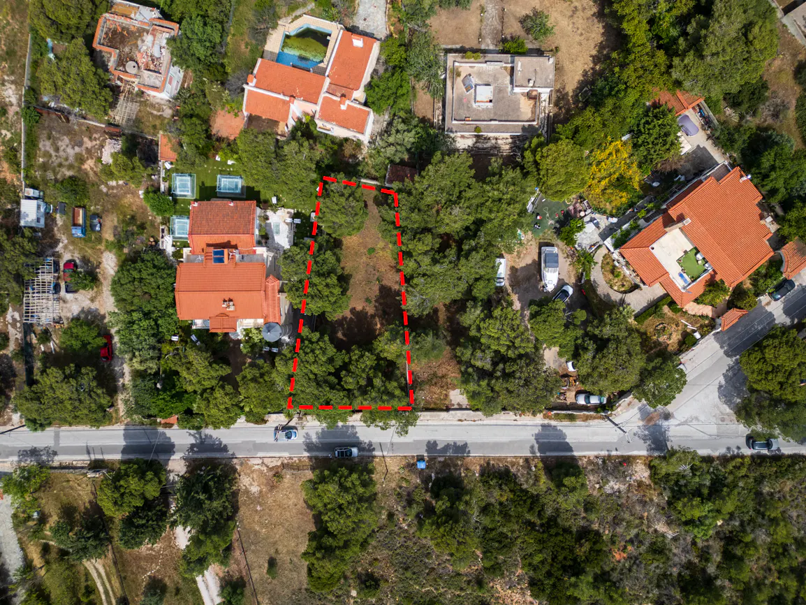 Aerial view of a vacant lot outlined in red, surrounded by trees and houses with red tile roofs.