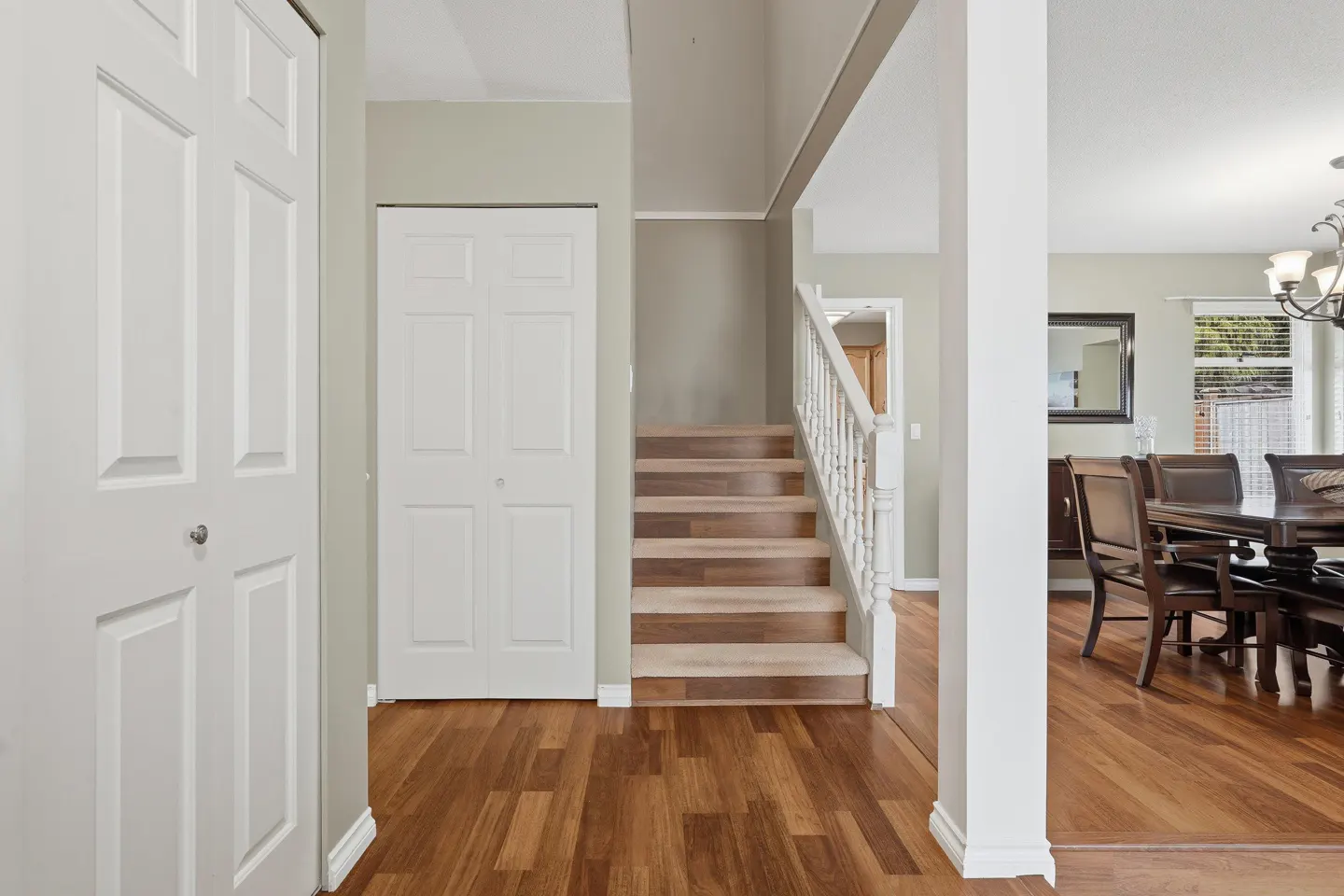 Foyer with hardwood floors, white closet doors, and stairs leading up. A dining room is visible through a white column.