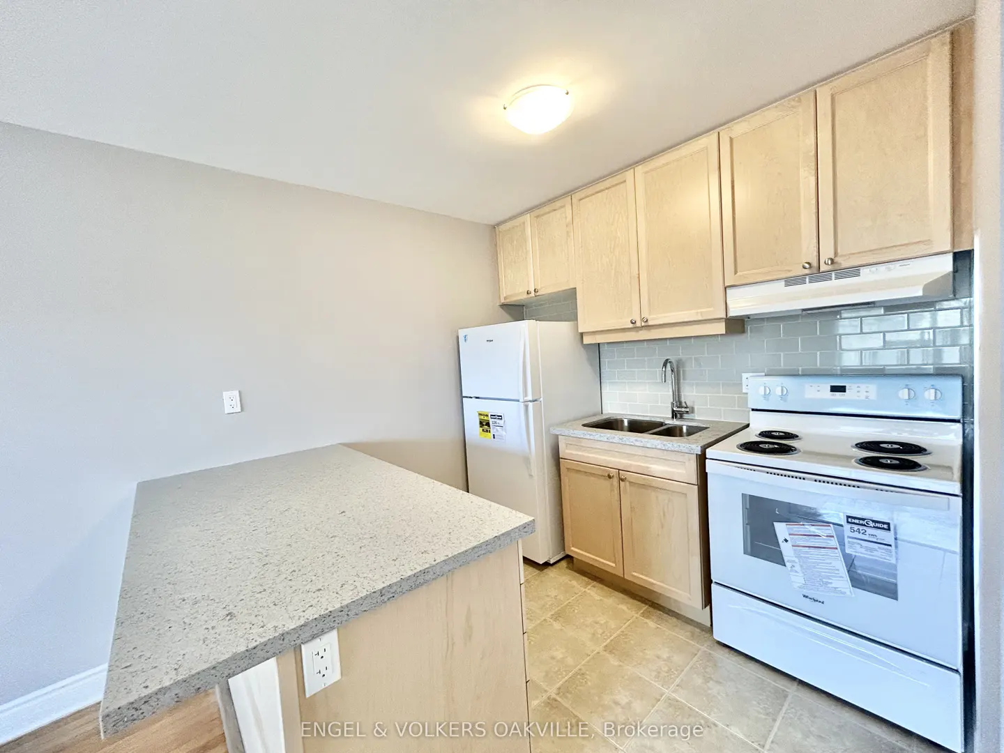 A bright kitchen with light wood cabinets, white appliances, and a speckled gray countertop.