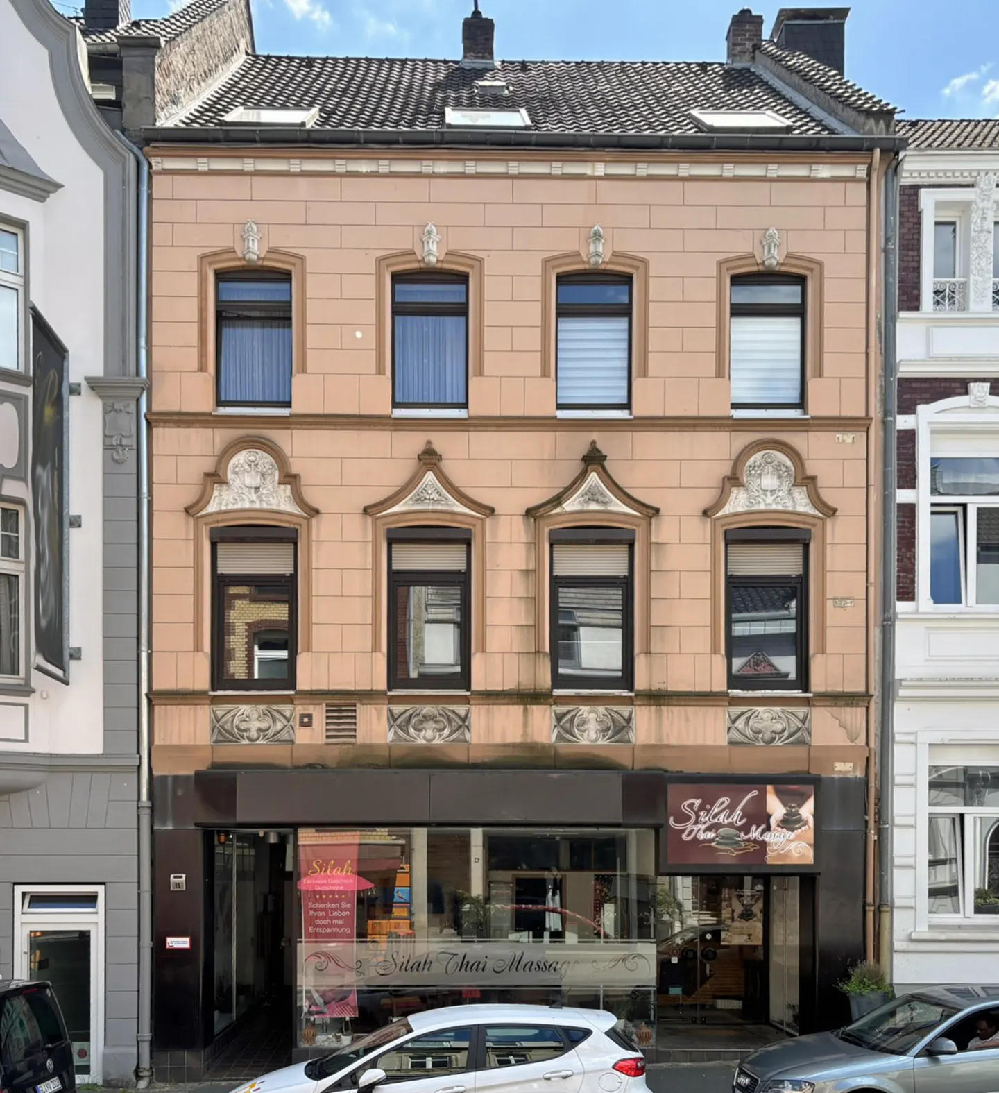 A three-story peach-colored building with a ground-floor storefront labeled "Silah Thai Massage" on a city street.